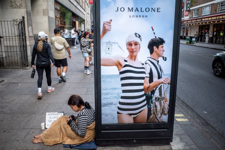 Candid street photography of a woman in a stripy top by an advert of a woman in stripy swimsuit on Charing Cross Road, London.